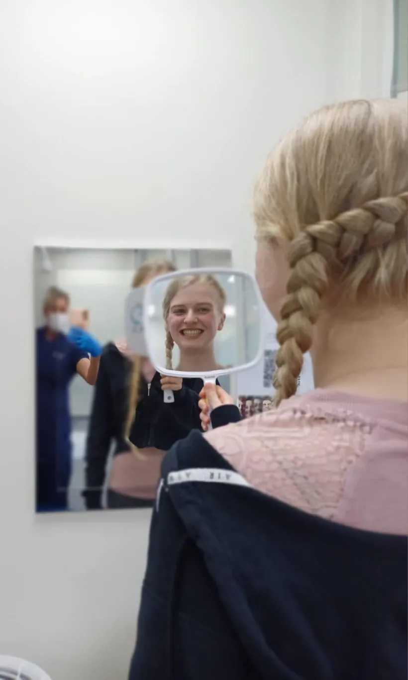 A young patient checking her new smile in the mirror at Pallant Advanced Dentistry